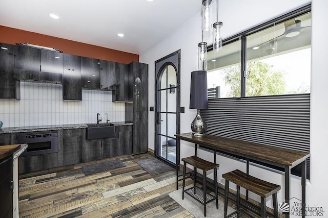 kitchen with decorative light fixtures, dark hardwood / wood-style flooring, tasteful backsplash, sink, and oven