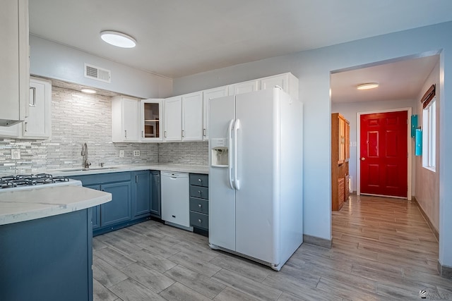 kitchen featuring white appliances, white cabinets, blue cabinets, sink, and tasteful backsplash