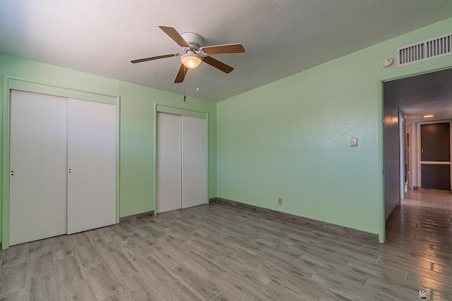 unfurnished bedroom featuring ceiling fan, light hardwood / wood-style floors, and multiple closets