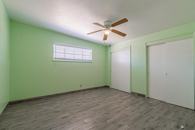 unfurnished bedroom with a textured ceiling, two closets, and ceiling fan