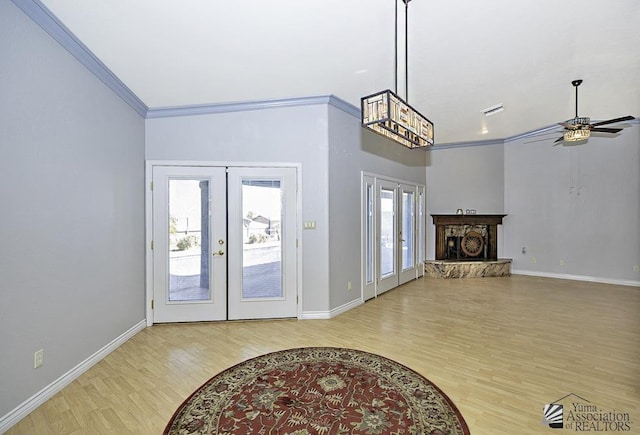 foyer entrance with crown molding, a stone fireplace, light hardwood / wood-style floors, and french doors