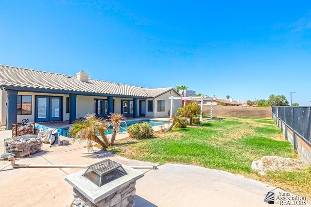 back of house with a fenced in pool, a lawn, an outdoor fire pit, a patio area, and french doors