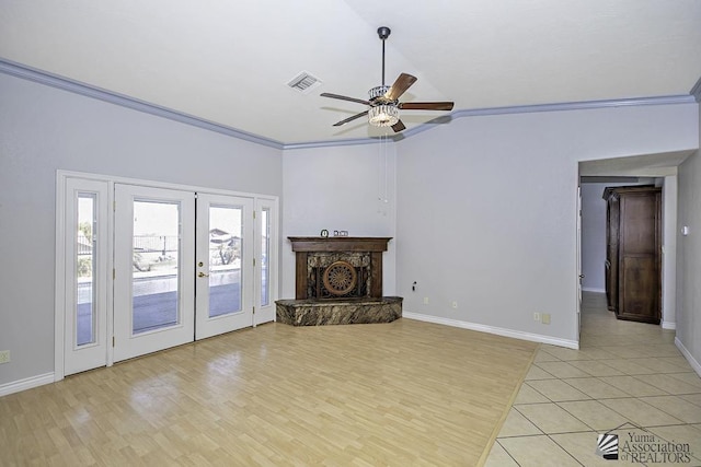 living room featuring light hardwood / wood-style flooring, ceiling fan, ornamental molding, a stone fireplace, and french doors