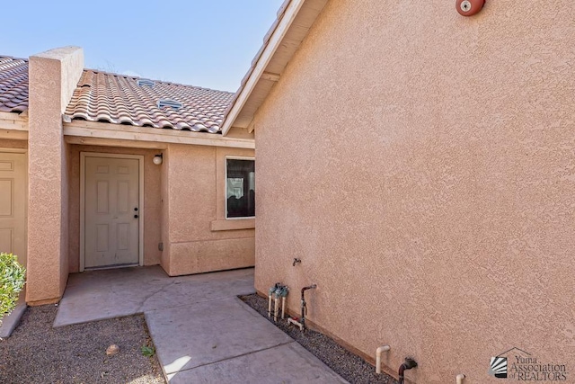 doorway to property with a tiled roof, a patio area, and stucco siding