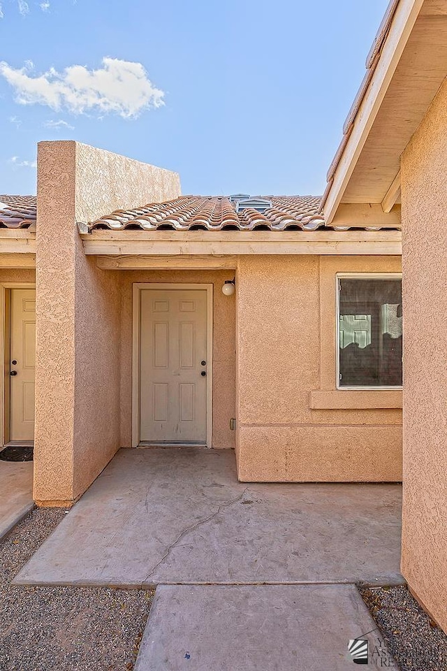 view of exterior entry with stucco siding and a tile roof