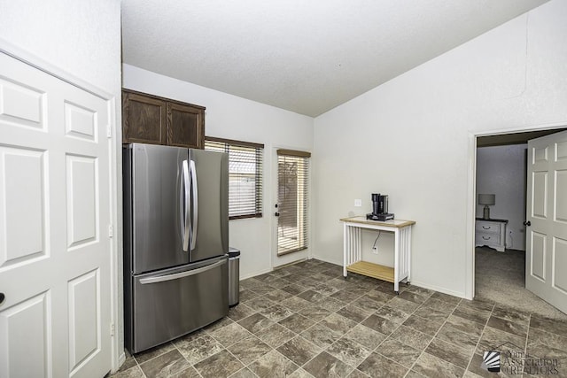 kitchen featuring lofted ceiling, stone finish floor, freestanding refrigerator, dark brown cabinetry, and baseboards