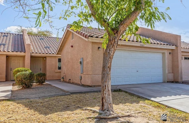 exterior space with concrete driveway, a tiled roof, an attached garage, and stucco siding