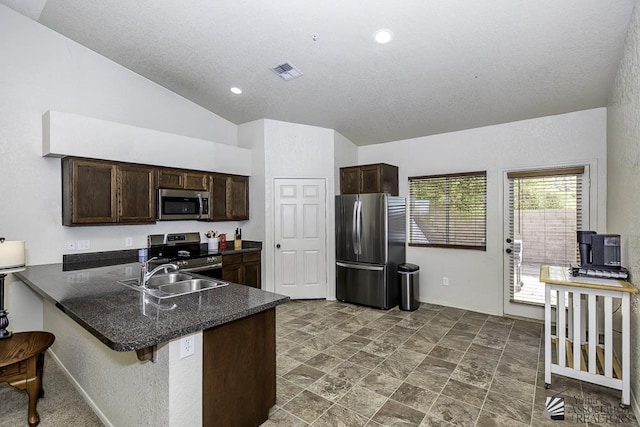 kitchen featuring dark countertops, dark brown cabinetry, appliances with stainless steel finishes, a peninsula, and a sink