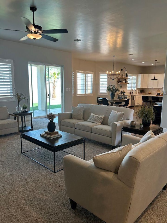 living room with sink, light colored carpet, and ceiling fan with notable chandelier