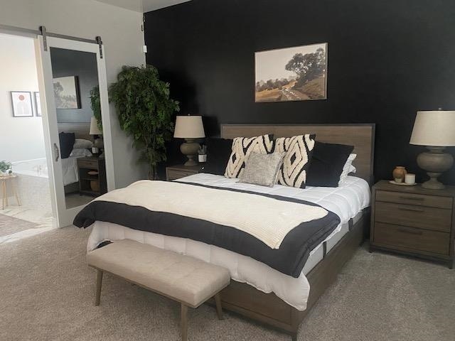 carpeted bedroom featuring a barn door and ensuite bath