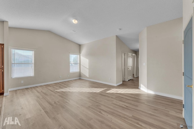 spare room with lofted ceiling, a textured ceiling, and light hardwood / wood-style flooring