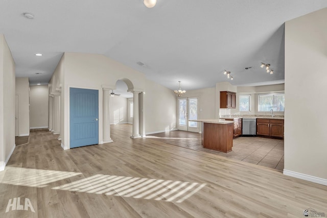 kitchen featuring lofted ceiling, sink, light wood-type flooring, dishwasher, and decorative columns