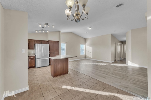 kitchen featuring lofted ceiling, light tile patterned floors, stainless steel refrigerator, a notable chandelier, and a kitchen island