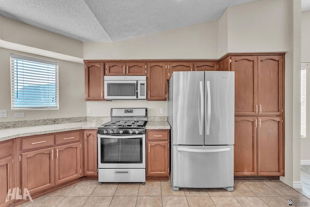 kitchen with light tile patterned flooring, lofted ceiling, appliances with stainless steel finishes, and a textured ceiling