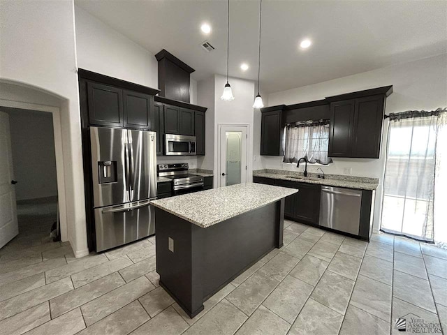 kitchen with light stone countertops, sink, stainless steel appliances, pendant lighting, and a kitchen island