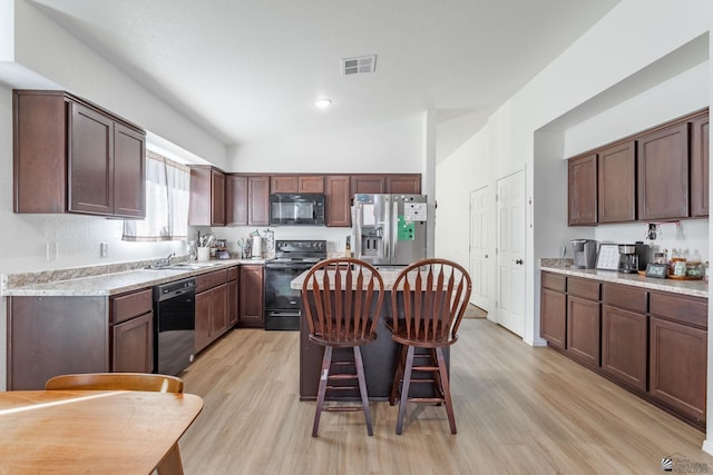 kitchen with sink, dark brown cabinetry, a breakfast bar area, and black appliances