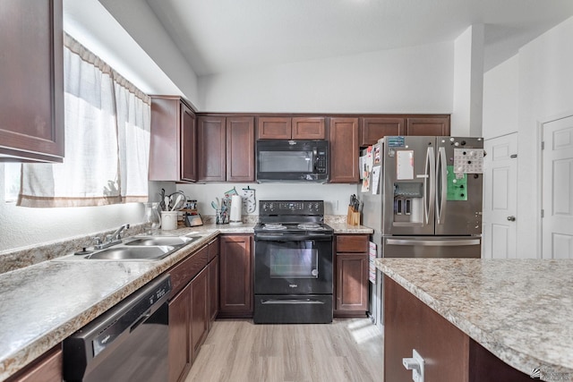 kitchen featuring black appliances, light hardwood / wood-style floors, a towering ceiling, and sink