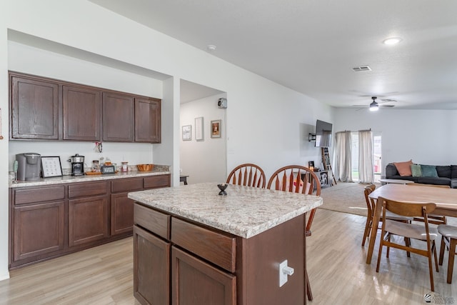 kitchen with ceiling fan, a kitchen island, dark brown cabinetry, and light wood-type flooring