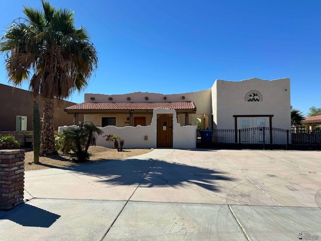 pueblo-style house with fence, a tiled roof, concrete driveway, stucco siding, and a gate