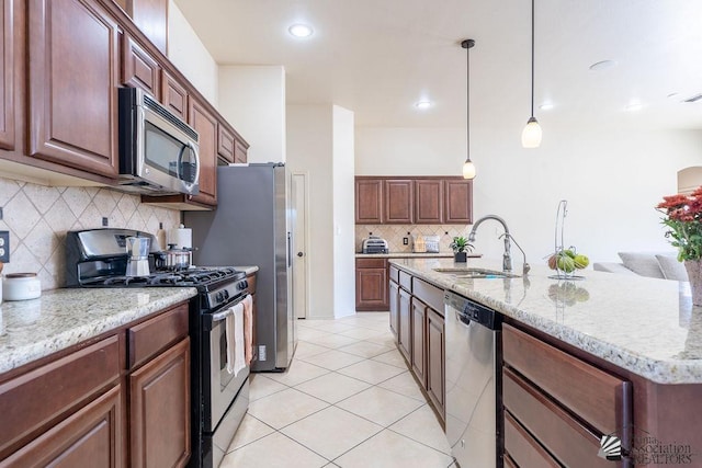 kitchen featuring stainless steel appliances, a kitchen island with sink, sink, light tile patterned floors, and hanging light fixtures