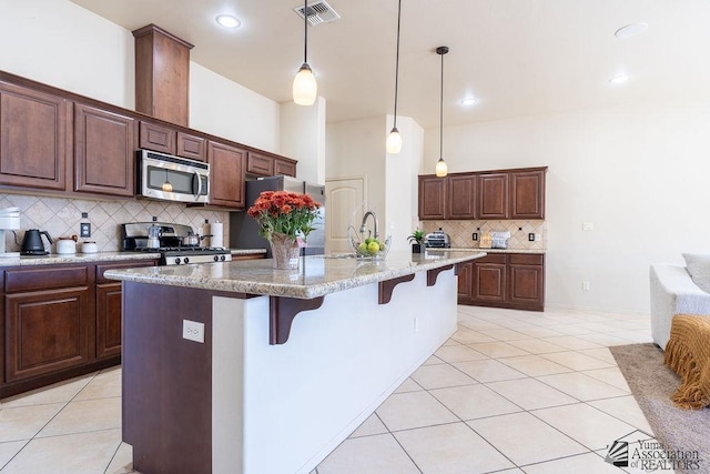 kitchen with pendant lighting, an island with sink, appliances with stainless steel finishes, tasteful backsplash, and a kitchen bar