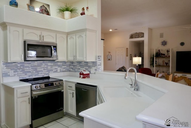 kitchen with a sink, light countertops, white cabinets, stainless steel appliances, and a peninsula