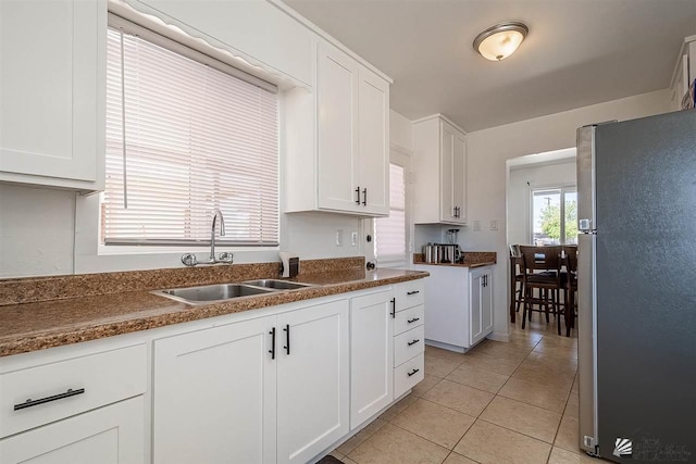 kitchen with white cabinets, light tile patterned floors, stainless steel refrigerator, and sink