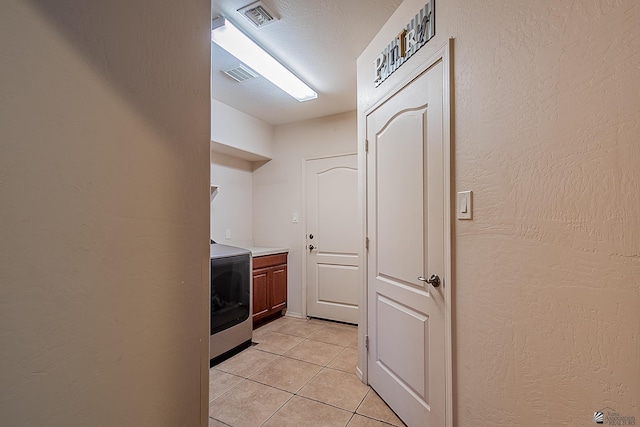 clothes washing area featuring visible vents, a textured wall, light tile patterned flooring, and washer / dryer