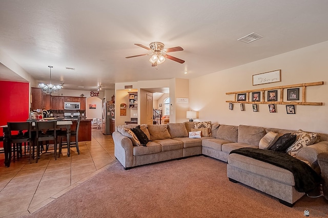 living area featuring light tile patterned floors, visible vents, and ceiling fan with notable chandelier