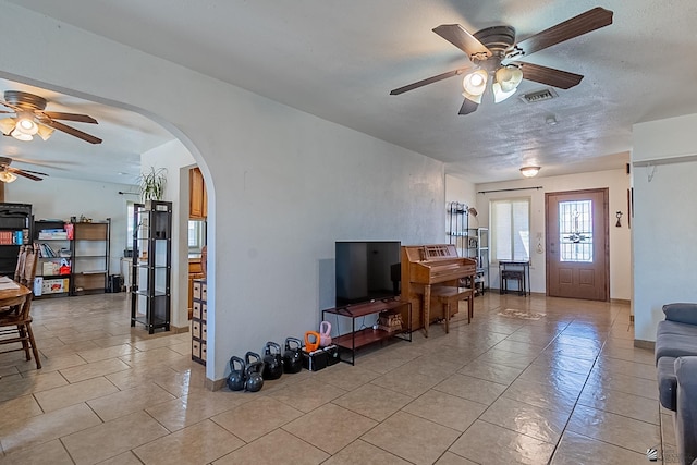 living room with visible vents, ceiling fan, light tile patterned floors, arched walkways, and a textured ceiling