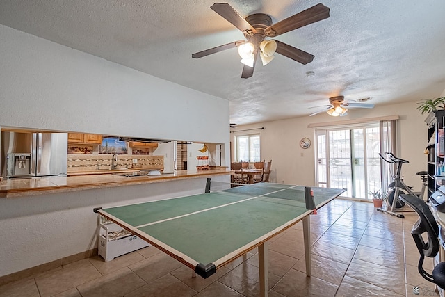 game room with light tile patterned floors, a textured wall, a textured ceiling, and a sink