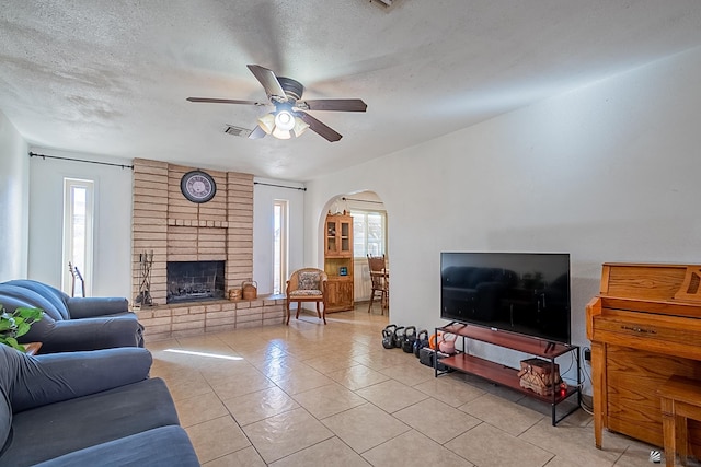 tiled living room featuring a textured ceiling, plenty of natural light, arched walkways, and ceiling fan