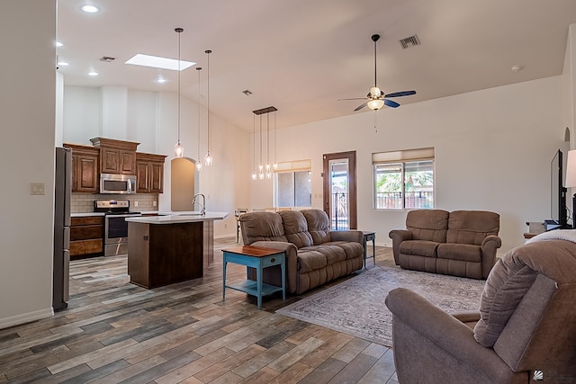 living room with visible vents, high vaulted ceiling, wood finished floors, a skylight, and ceiling fan