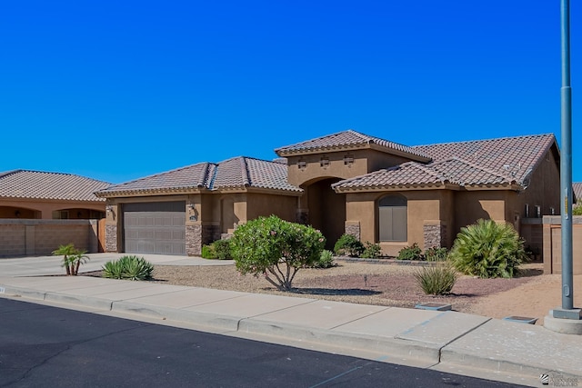 mediterranean / spanish house with stucco siding, concrete driveway, a garage, stone siding, and a tile roof