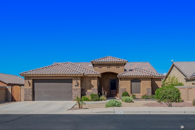 mediterranean / spanish house with stucco siding, driveway, a tile roof, stone siding, and a garage