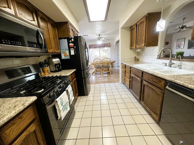 kitchen with light tile patterned floors, arched walkways, a ceiling fan, stainless steel appliances, and a sink