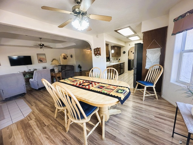 dining area with arched walkways, ceiling fan, light wood finished floors, and baseboards