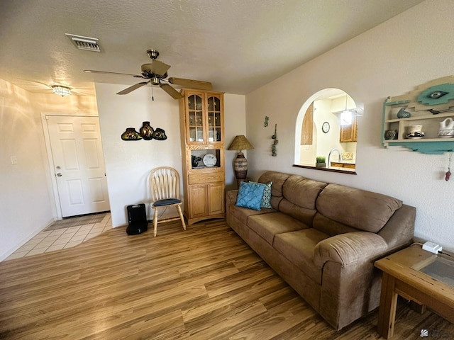 living room featuring light wood-style flooring, visible vents, ceiling fan, and a textured ceiling