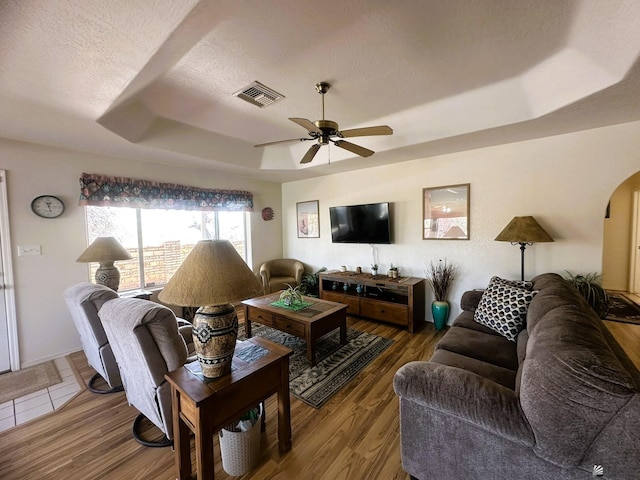 living room featuring arched walkways, a tray ceiling, wood finished floors, and visible vents