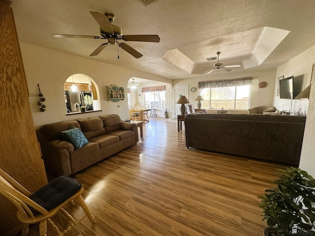 living room with a textured ceiling, arched walkways, wood finished floors, visible vents, and a tray ceiling