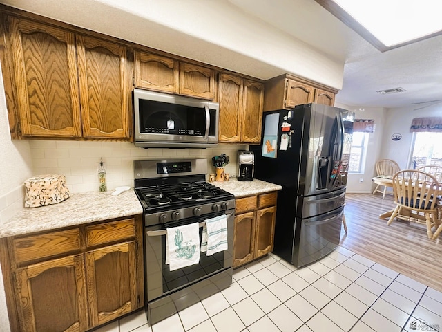 kitchen featuring visible vents, decorative backsplash, appliances with stainless steel finishes, brown cabinets, and light countertops