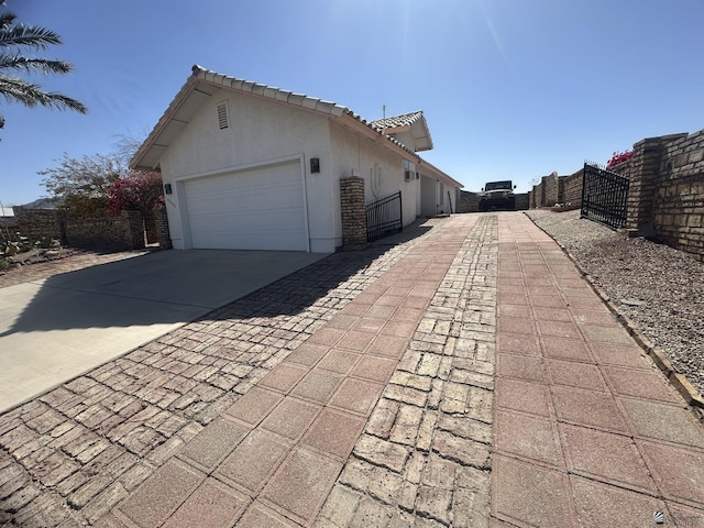 view of side of property with an attached garage, fence, driveway, a tiled roof, and stucco siding