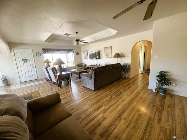 living area featuring visible vents, arched walkways, a ceiling fan, wood finished floors, and a tray ceiling