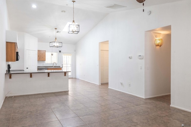 kitchen with brown cabinets, decorative light fixtures, a breakfast bar area, dark countertops, and a sink