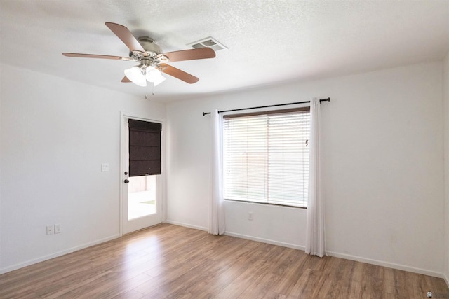 spare room featuring a textured ceiling, a ceiling fan, visible vents, baseboards, and light wood-type flooring