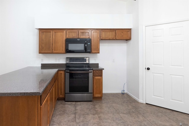 kitchen featuring dark countertops, black microwave, brown cabinetry, and electric stove