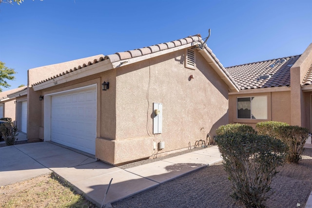 view of home's exterior featuring a garage, driveway, a tile roof, and stucco siding