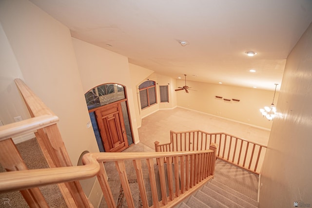 stairs with carpet floors and ceiling fan with notable chandelier