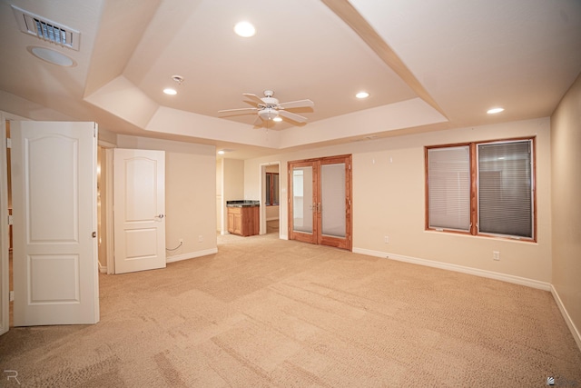 spare room with french doors, ceiling fan, a tray ceiling, and light carpet