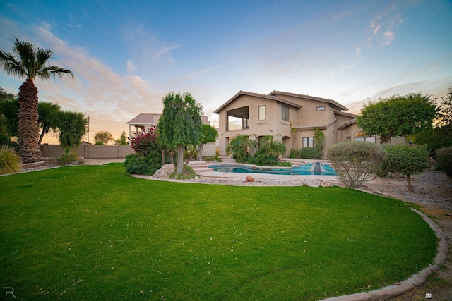 back house at dusk featuring a fenced in pool, a balcony, and a lawn